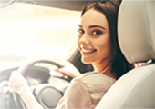 Foto de uma mulher sorridente sentada ao volante de um carro, olhando para trs